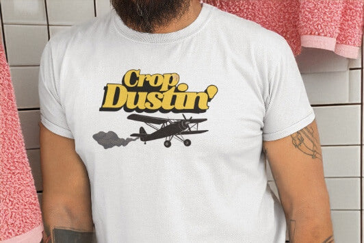 Person wearing a white t-shirt with 'Crop Dustin' graphic design in a bathroom.